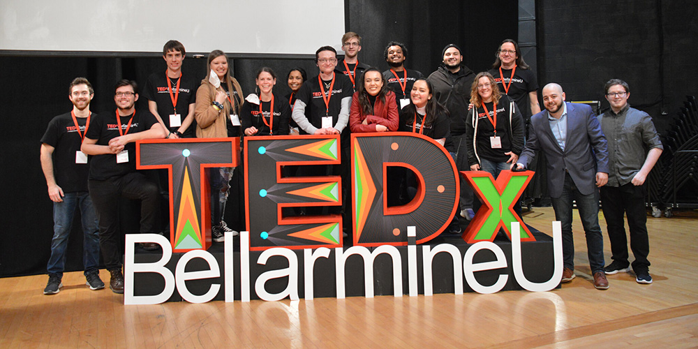 A large group of people beside a TEDx Bellarmine sign