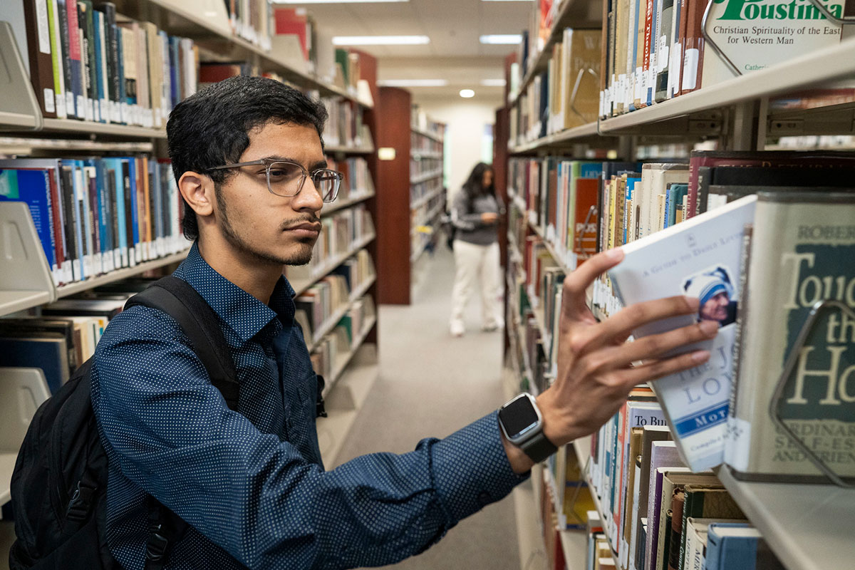 student pulls a book from a shelf in the library