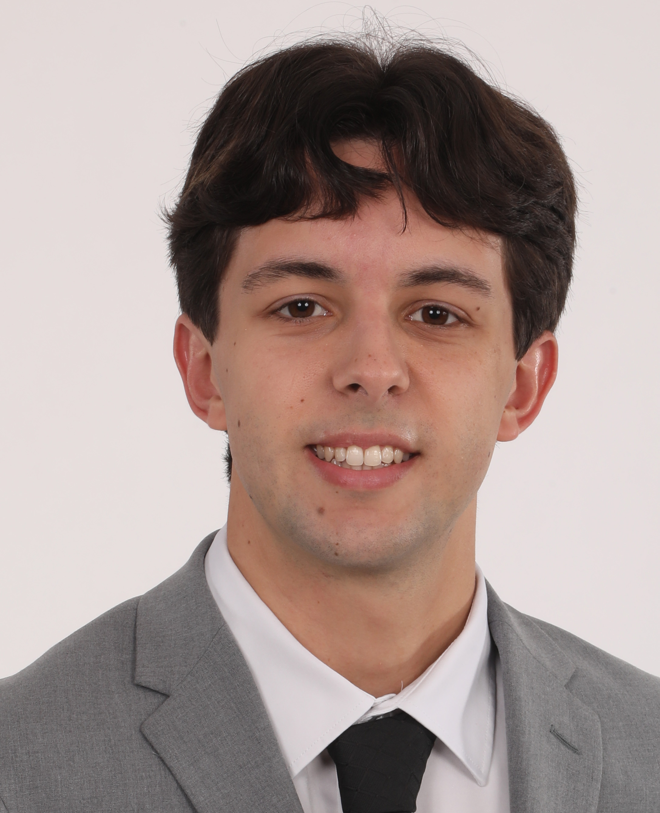 Nick Mugnaini Portrait of a young man in a gray suit, white shirt, and black tie against a plain light background